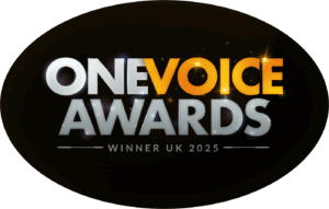 An oval shaped badge with a black background. 'One Voice Awards - Winner UK 2025' is in silver lettering with the exception of the word 'Voice' which is in sparkling gold. Scott won the One Voice Award 2025 for Best UK Male Voiceover Performance in a Television / Web Commercial.